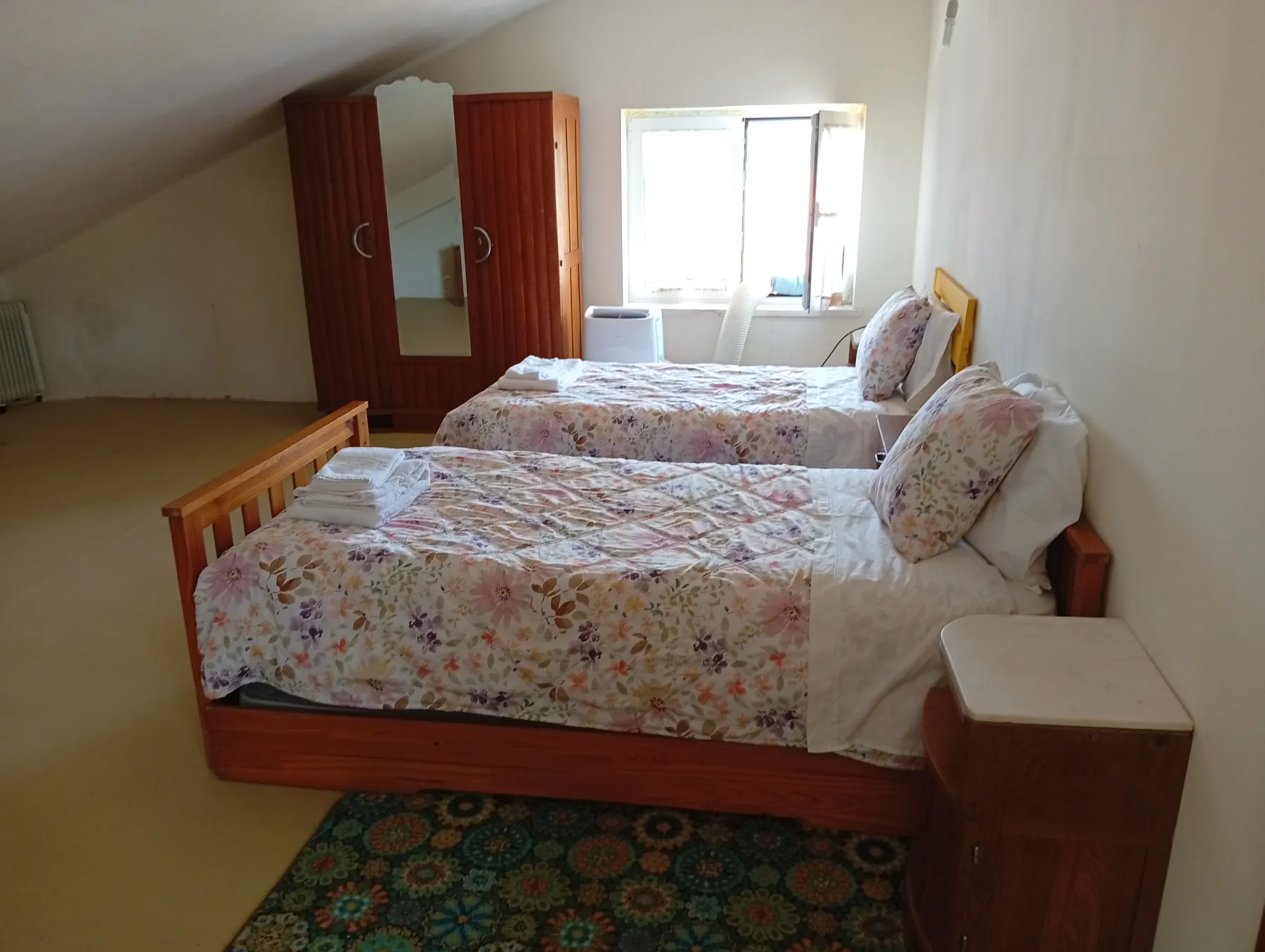 Vista ampla do quarto twin com guarda-fatos clássico em madeira, janela luminosa e camas compridas